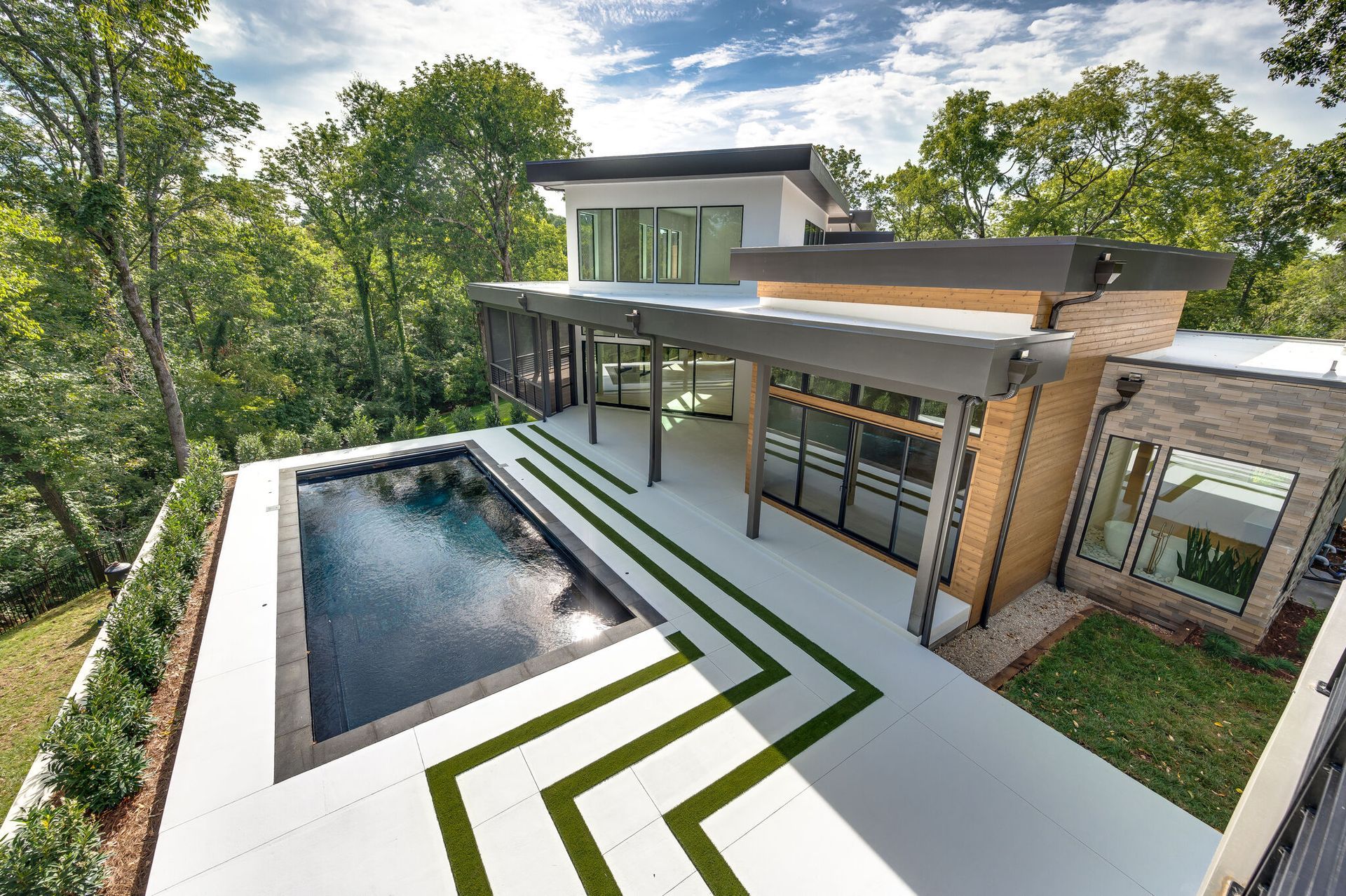 A modern house with a large swimming pool in the backyard surrounded by trees.