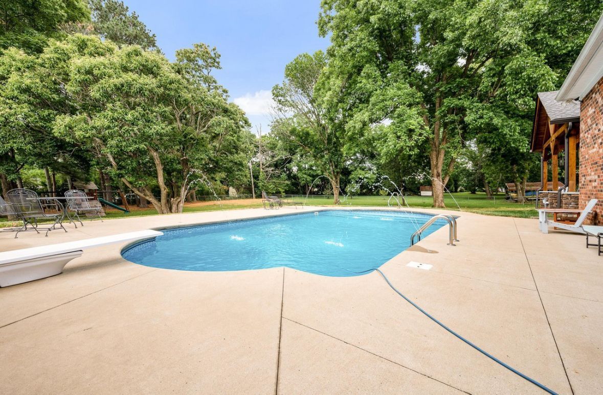 There is a large swimming pool in the backyard of a house surrounded by trees.