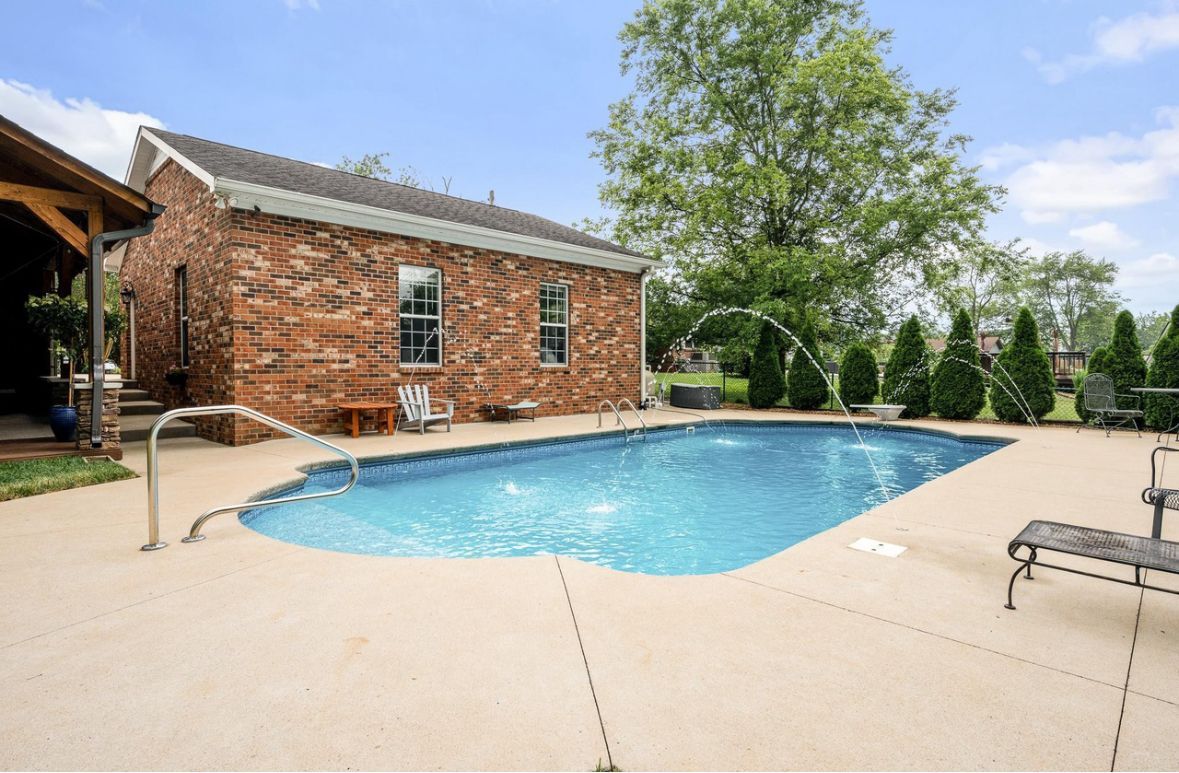 A large swimming pool is in front of a brick house.