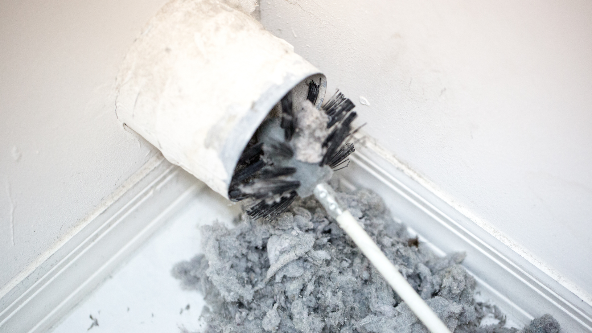 A vacuum cleaner is being used to clean a dryer duct.