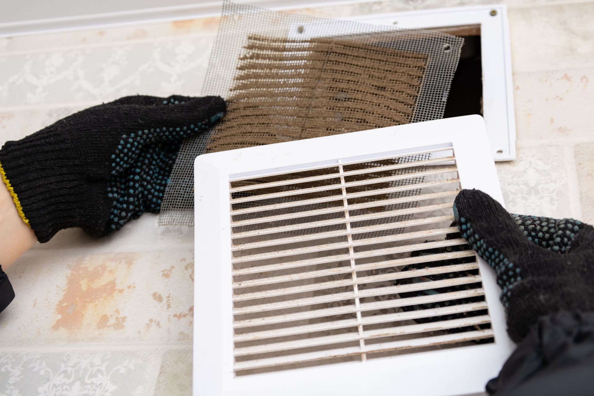 A person wearing gloves is cleaning a dirty air vent.