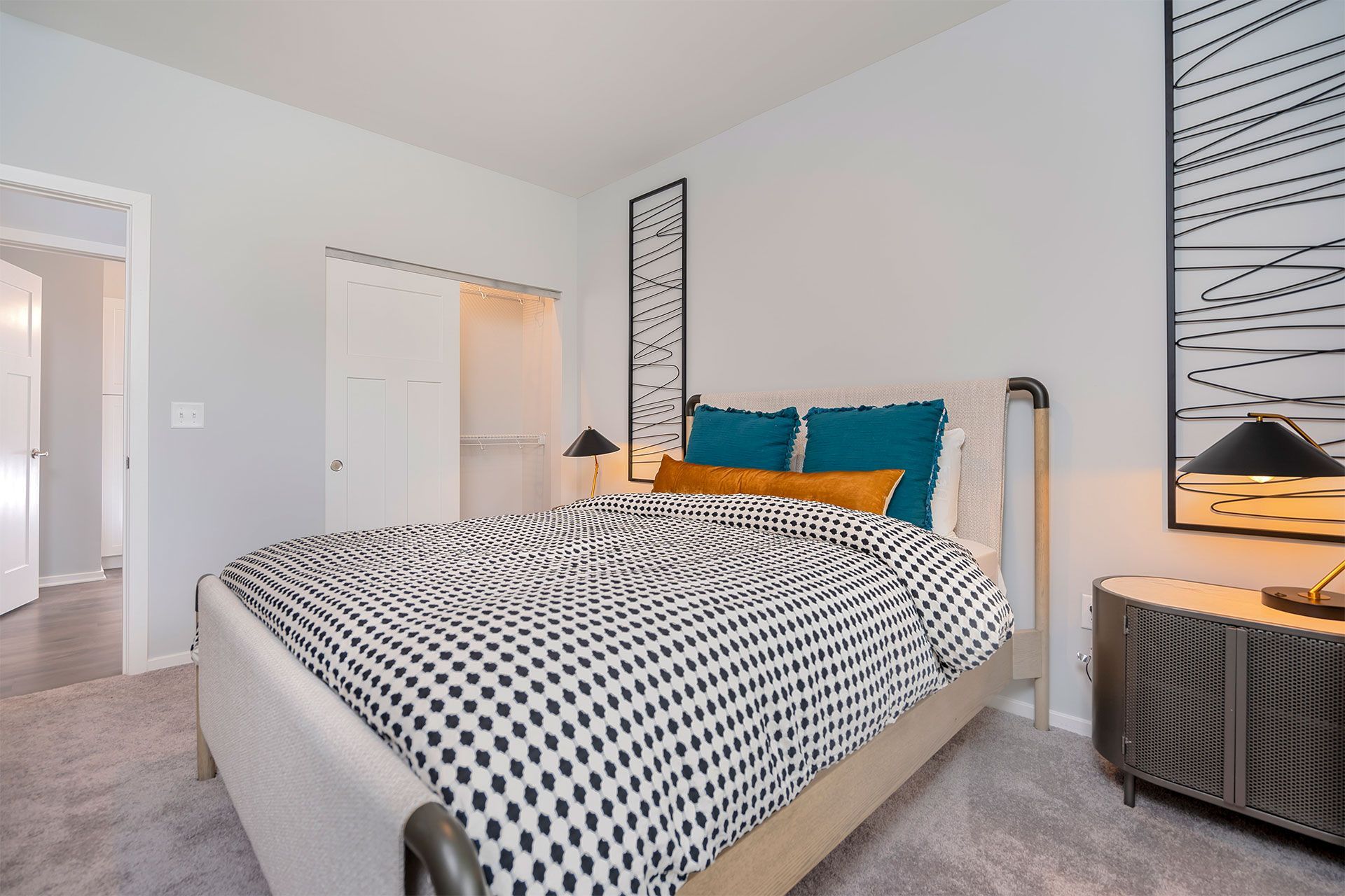 Bedroom with a large bed, patterned duvet, teal pillows, and decorative wall panels.