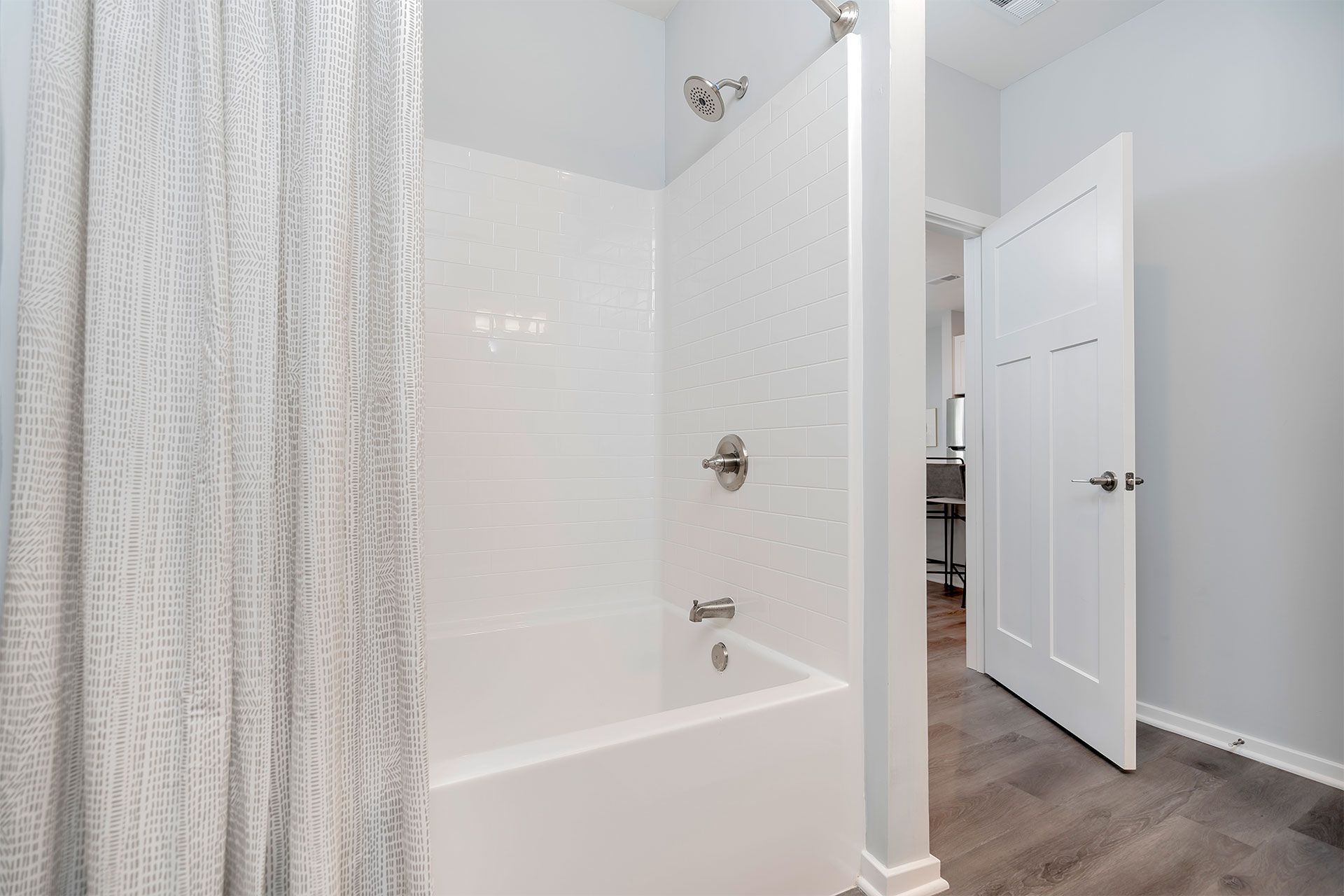 White-tiled bathroom shower with bathtub and a gray patterned curtain.