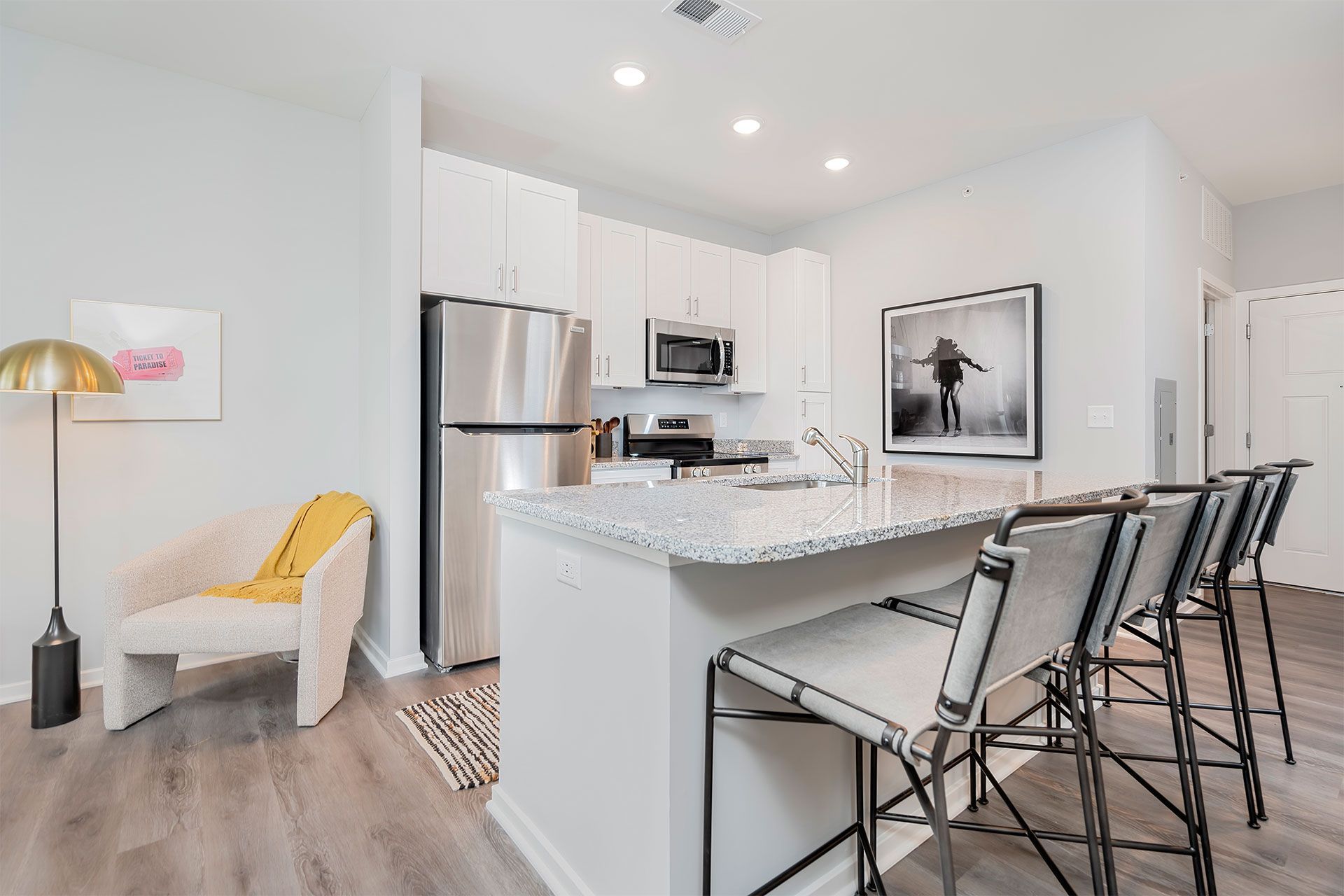 Open-concept kitchen in a modern apartment with granite island, white cabinets, and stainless appliances.
