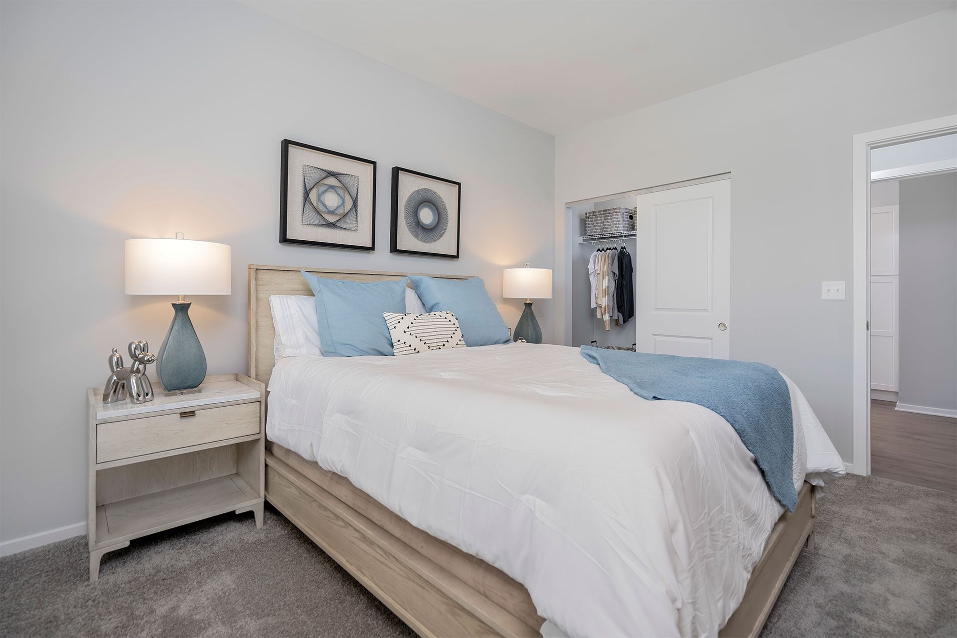 Bedroom with a light wood bed, blue pillows, matching lamps, and an open closet.
