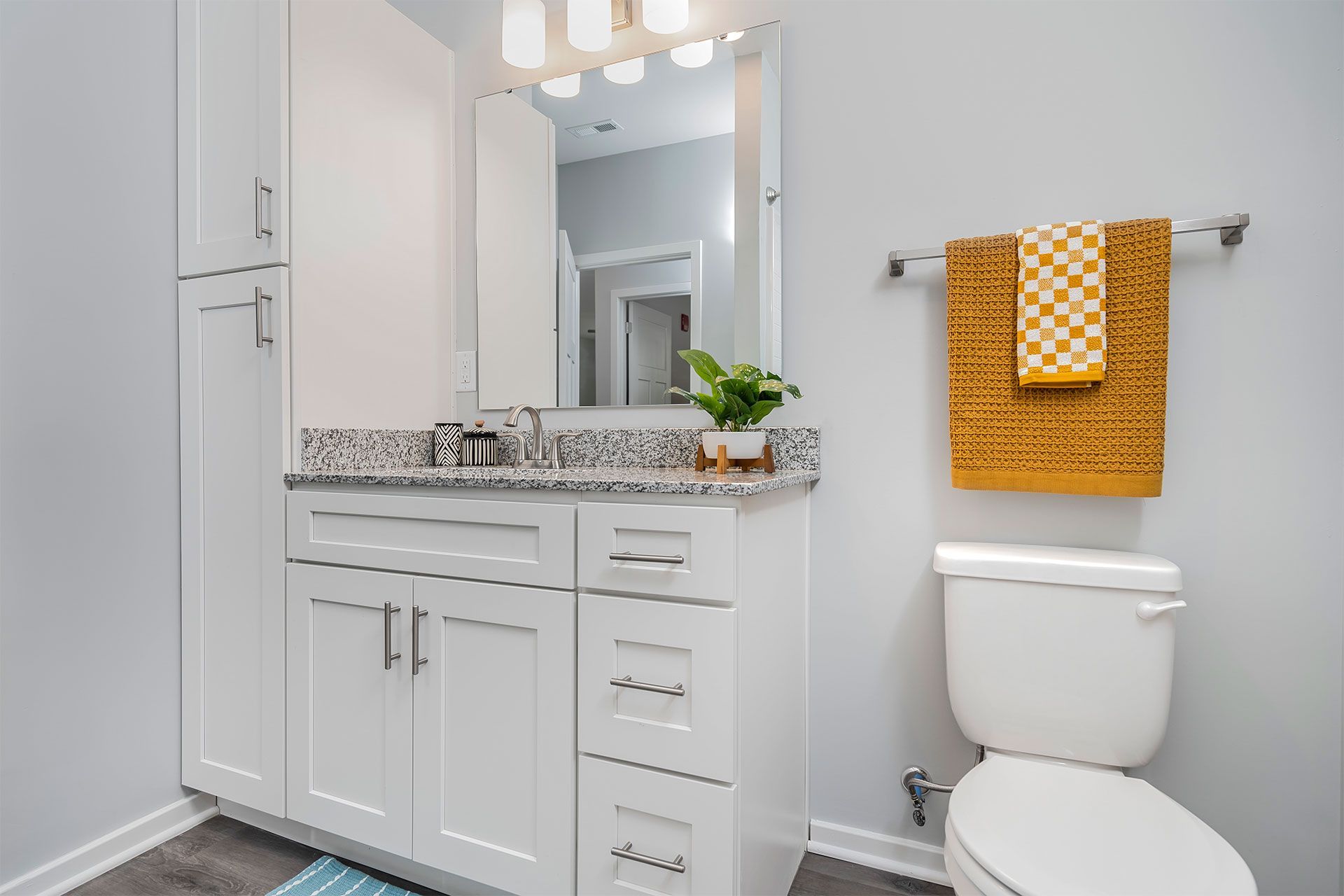 Modern apartment bathroom with white vanity, granite countertop, mirror, and yellow towel.