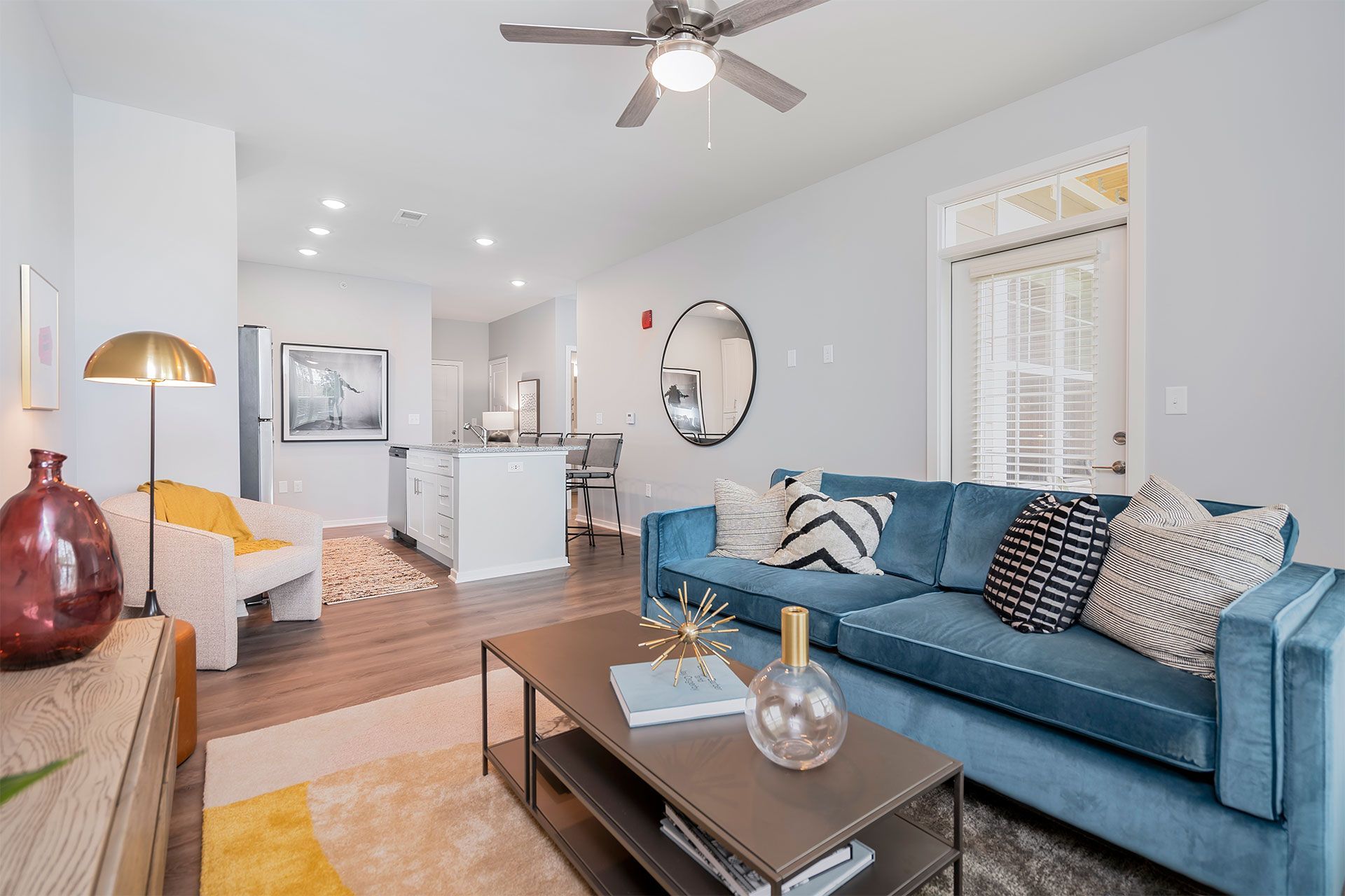 Open-concept living area with blue sofa, kitchen island, and ceiling fan.