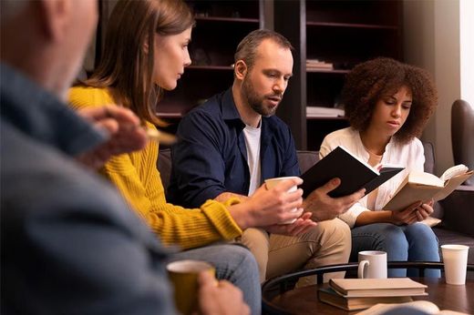 A group of people are sitting around a table reading books.