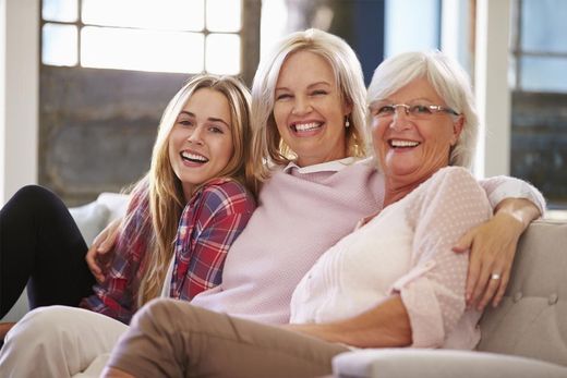 Three women are sitting on a couch and smiling for the camera.