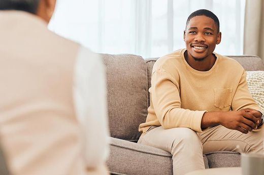 A man is sitting on a couch talking to another man.