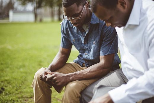 Two men are sitting on the grass looking at a cell phone.