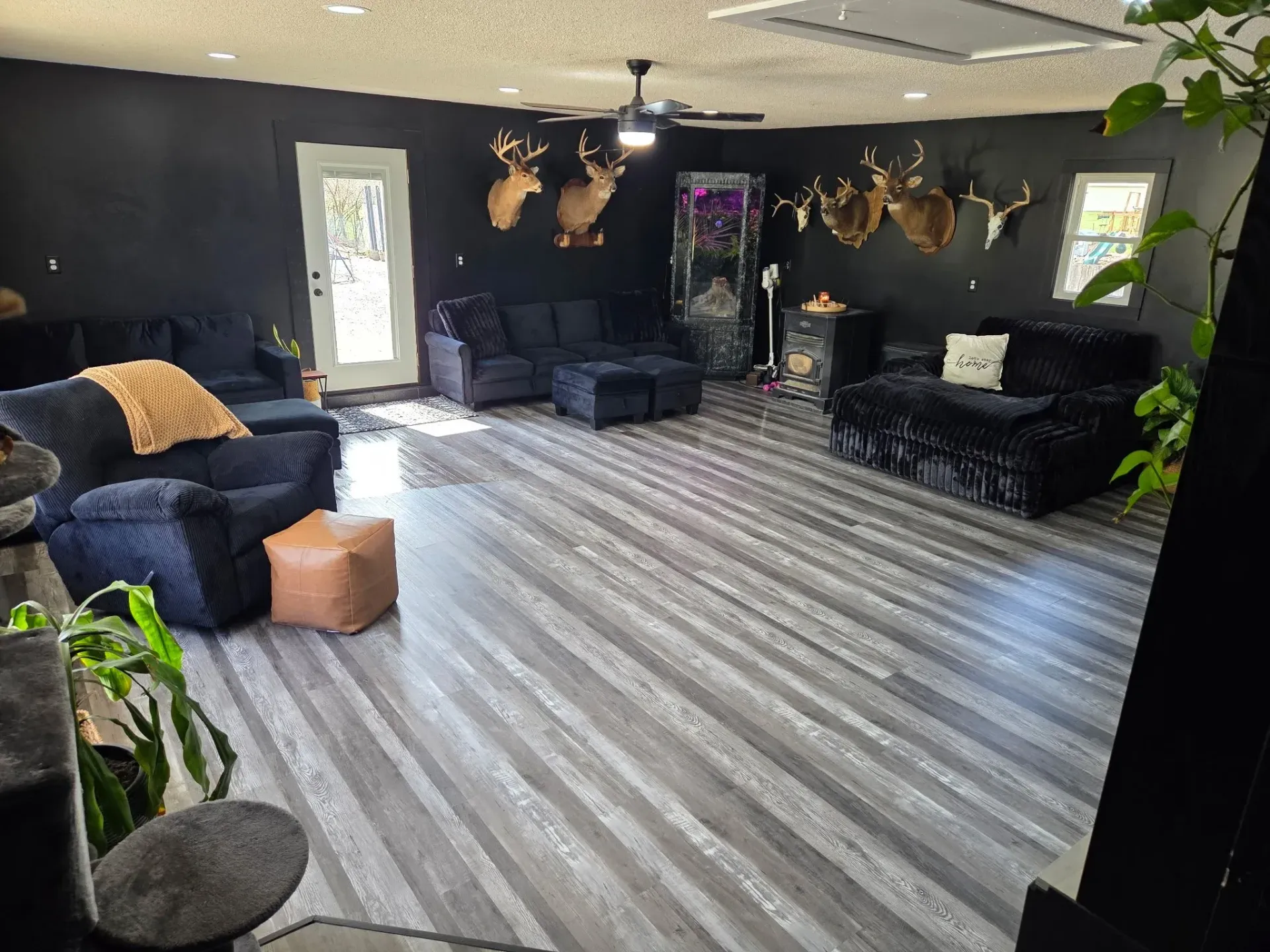 Dark-walled living room with grey wood-look floors, black furniture, and deer head mounts.