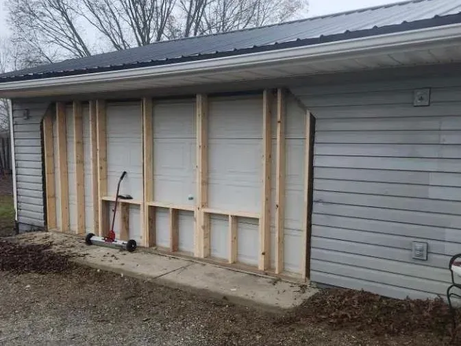 Garage undergoing renovation; exposed wooden framing where the garage door was, on a gray building.