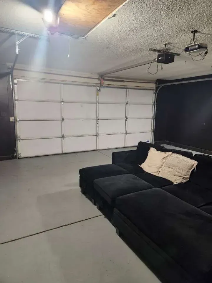 Garage converted into a living space; black sectional sofa, closed garage door, and a projector.