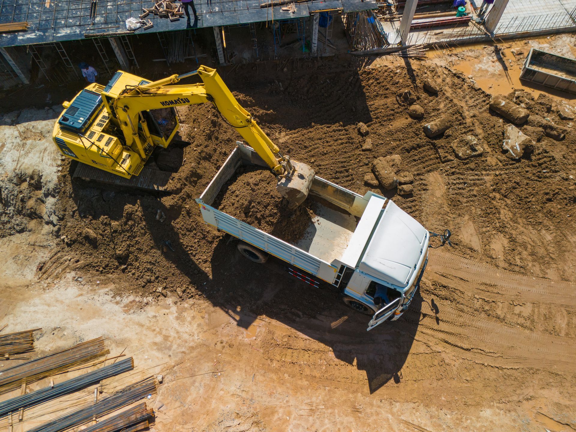 Yellow excavator loading dirt into a white dump truck at a construction site.