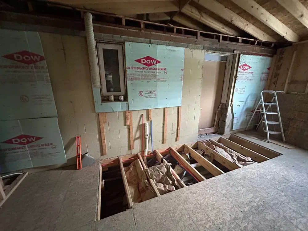 Renovation of a room with exposed beams, insulation, and floor joists. A small window is visible.