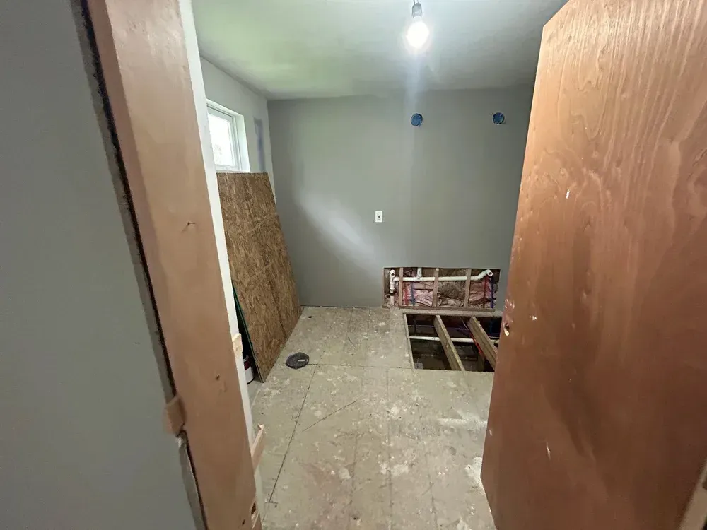 Bathroom under renovation with exposed floor joists and gray walls.