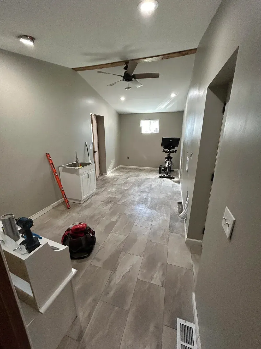 Room with new tile floor, tan walls, and a white sink. Construction tools are visible.