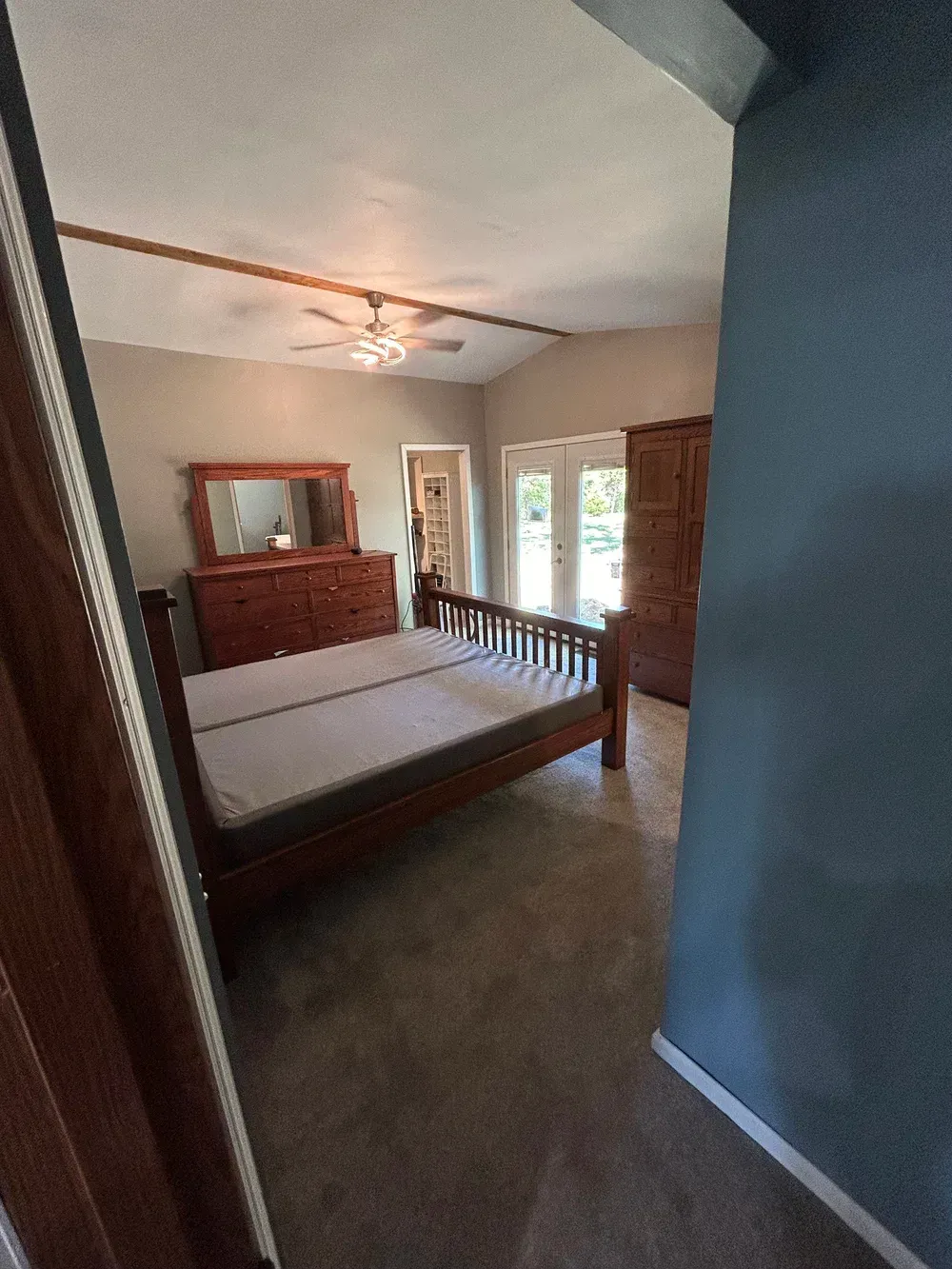 Bedroom with a wooden bed, dresser, and wardrobe, and a door leading to the outdoors.