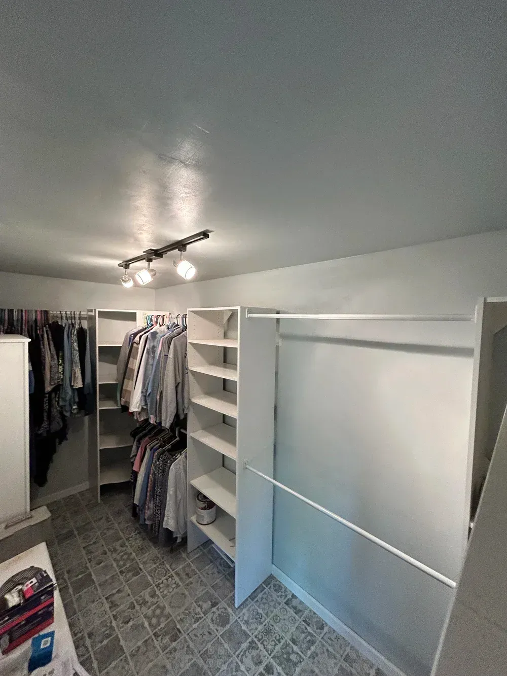 Walk-in closet with white shelving, racks of clothes, and a gray tiled floor.