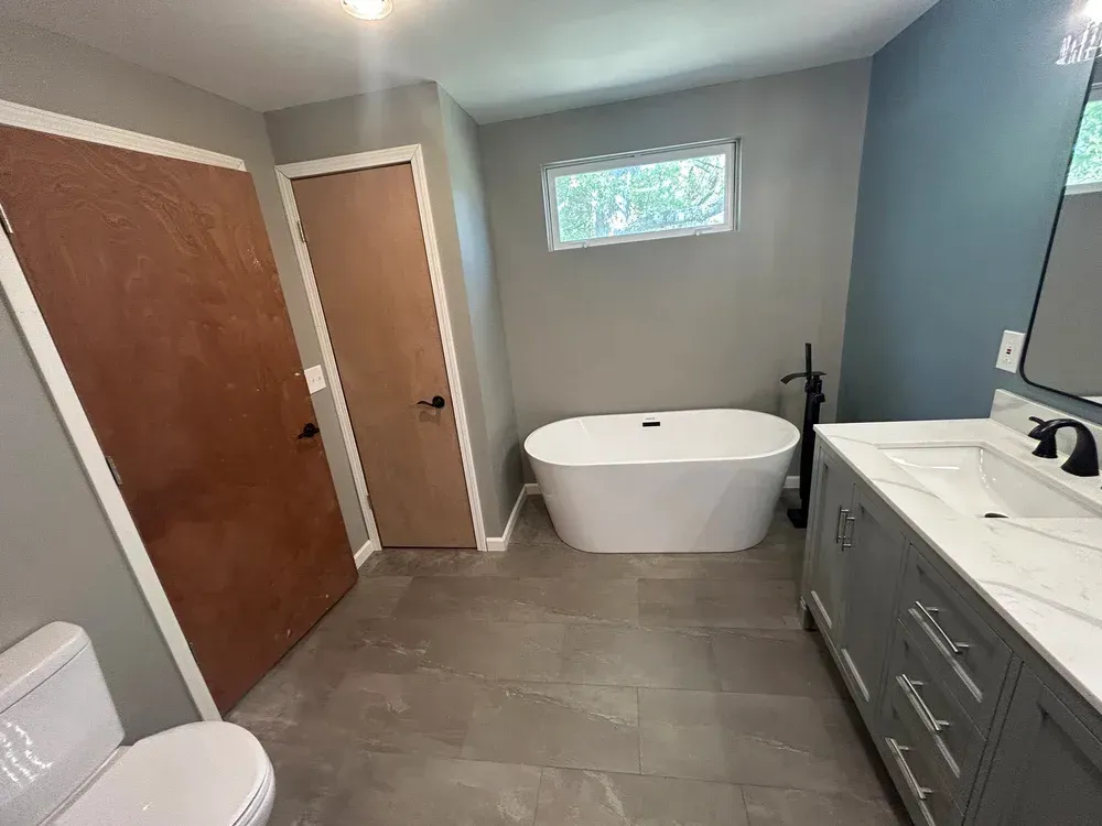 Modern bathroom with freestanding tub, gray vanity, and gray tile flooring.
