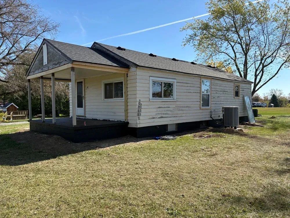 Single-story house with a porch and a new roof, on a grassy lot under a blue sky.
