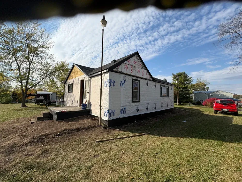House under renovation with new siding on a grassy lot under a blue sky.
