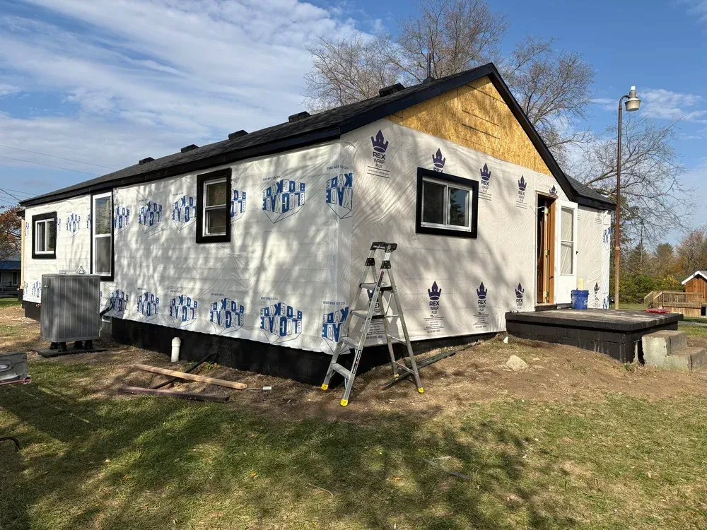 House under construction with white wrap, black trim, and a ladder on the lawn.