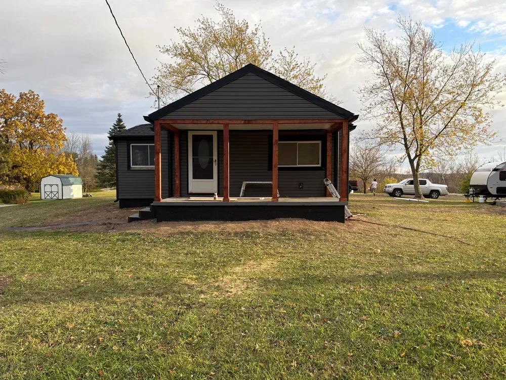 Small dark gray house with porch, brown trim, on grassy lawn, with trees.
