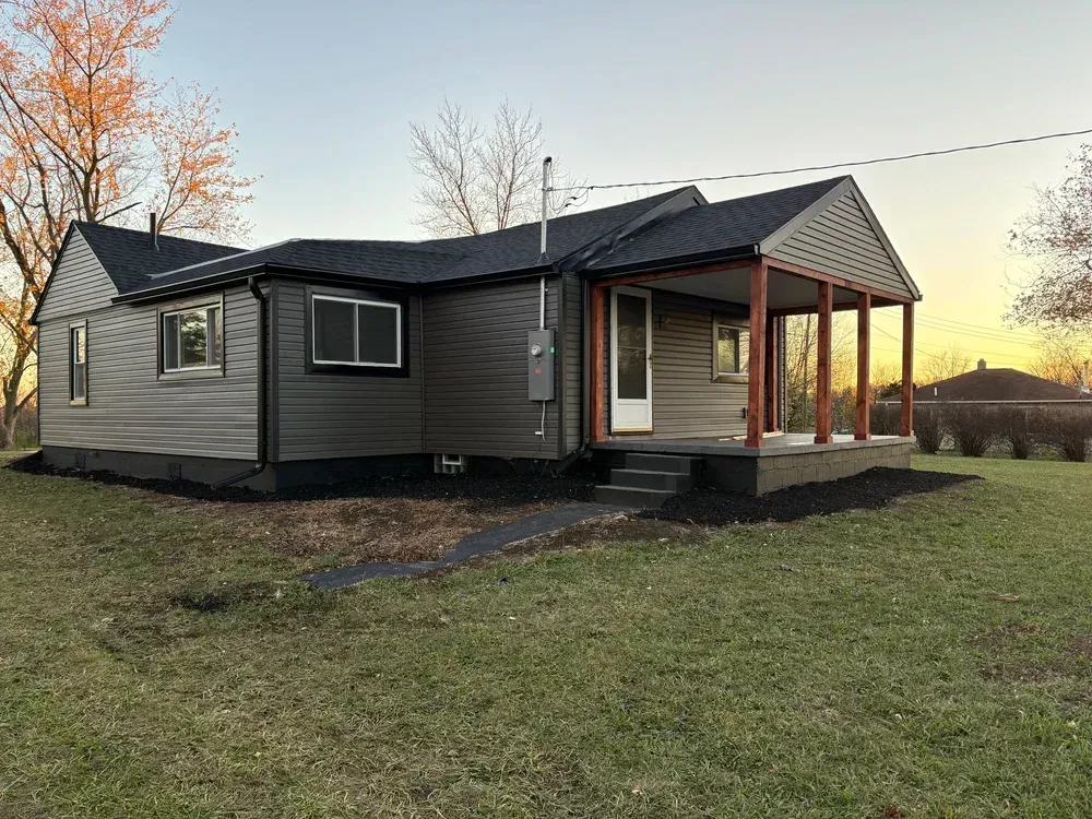 A small, gray house with a porch, set on a grassy lot at dusk.