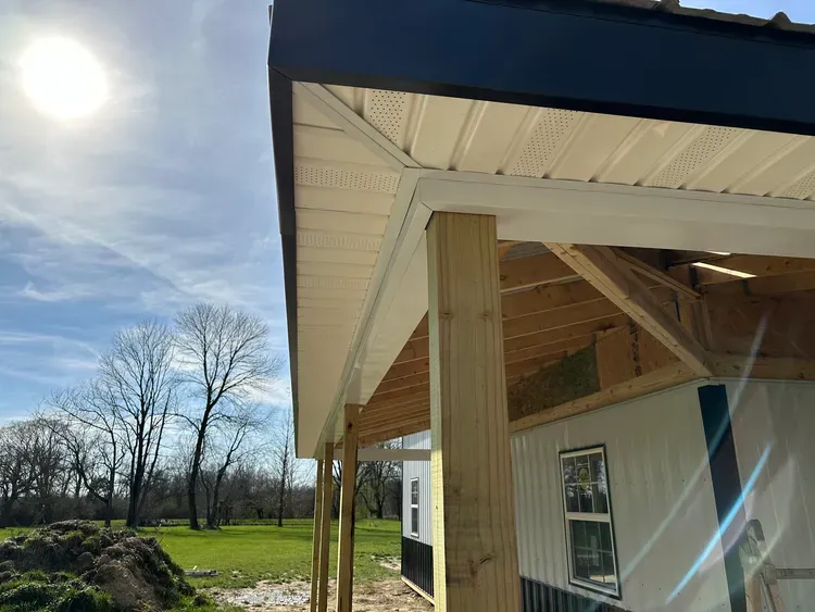 A building under construction with white siding and a covered porch, sunny day.