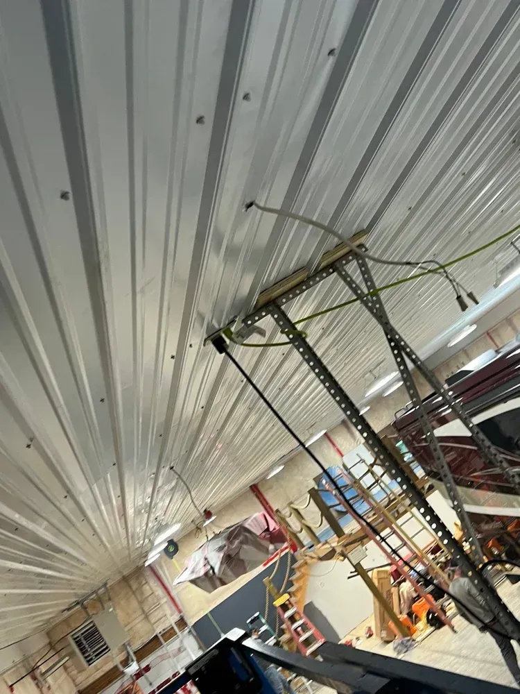 White metal ceiling with electrical wiring; a work area with a lift is below.
