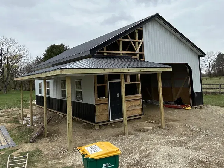 A partially built shed-like structure is attached to a white barn with a black roof. Construction materials are visible.
