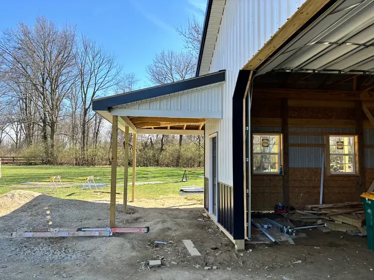 Construction site with white and black barn, porch, and trees.