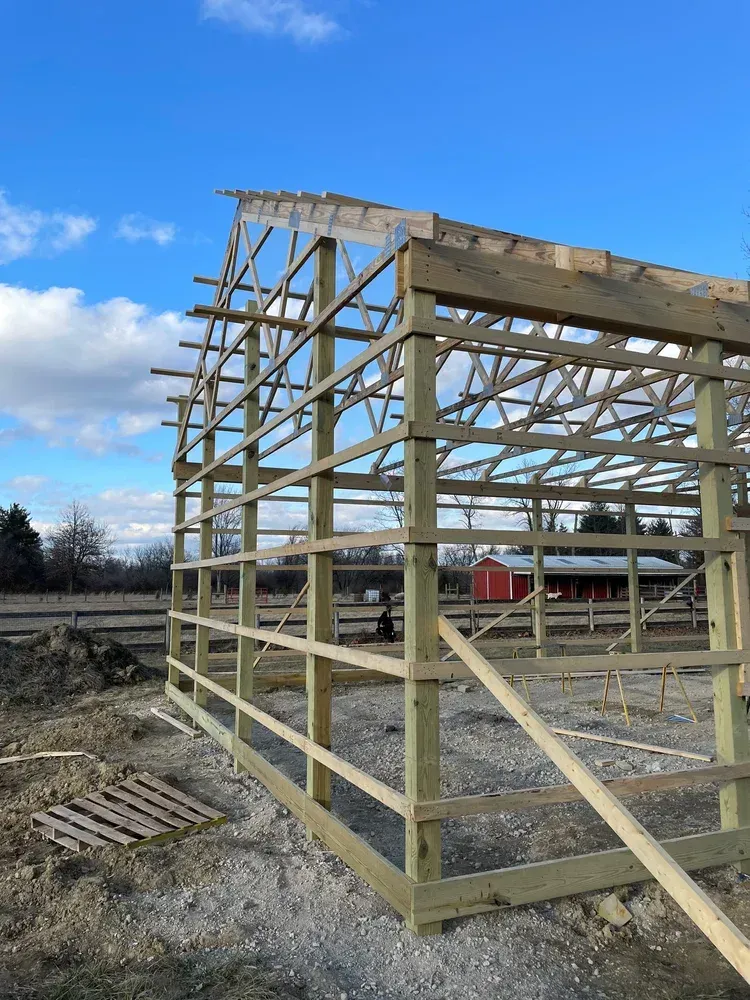 Framed barn under construction, wooden beams against a blue sky.