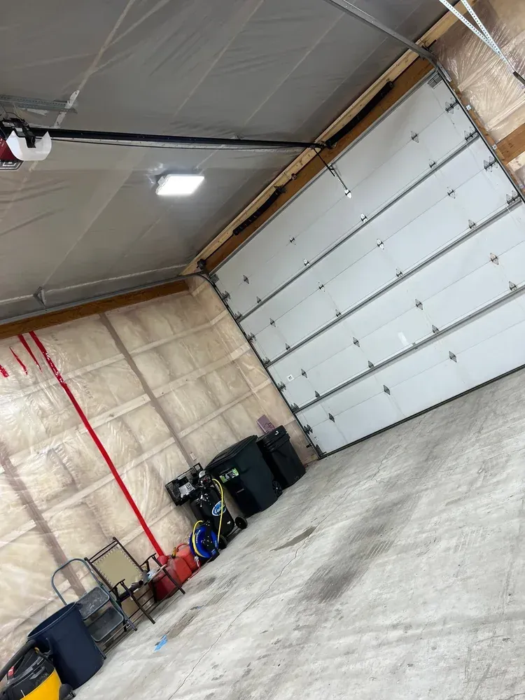 Garage interior with a partially open white garage door, insulation, and equipment.