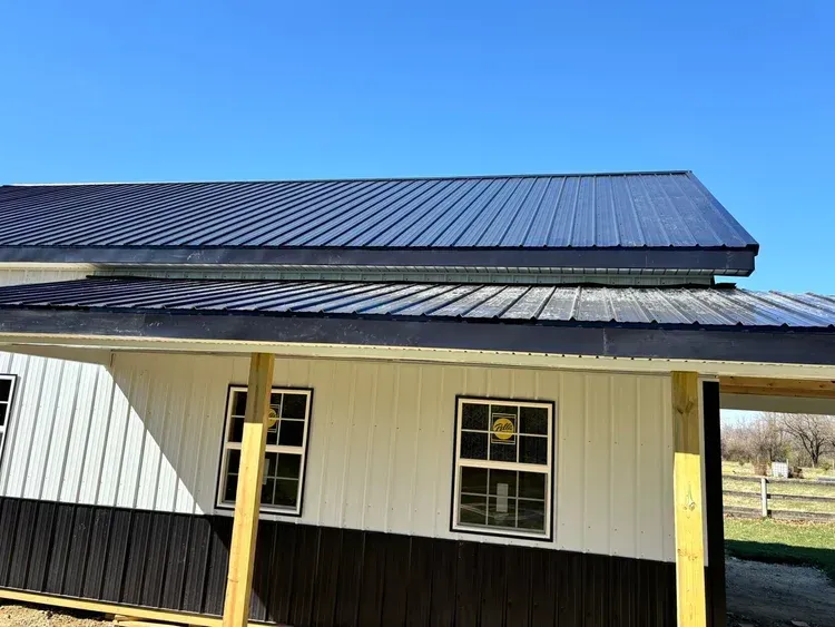 Black and white building with a dark metal roof against a clear blue sky.