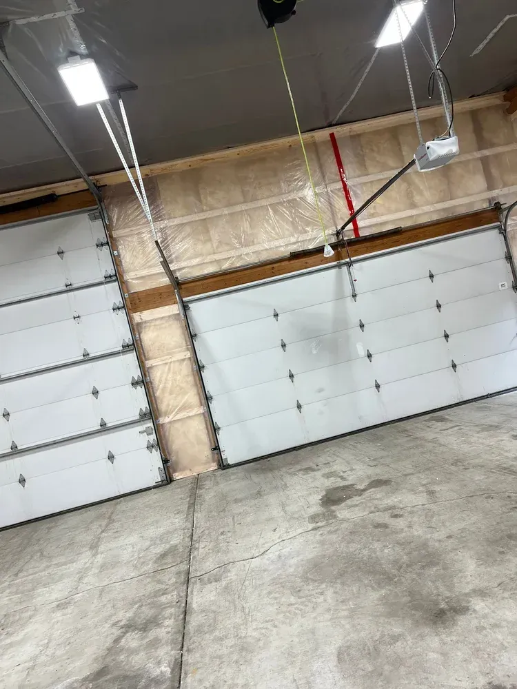 Two white garage doors in a concrete building, with a ceiling and insulation visible.