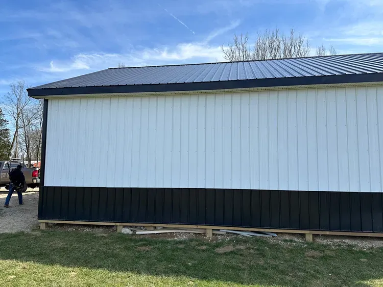 A white and black barn under a blue sky with a person standing nearby.