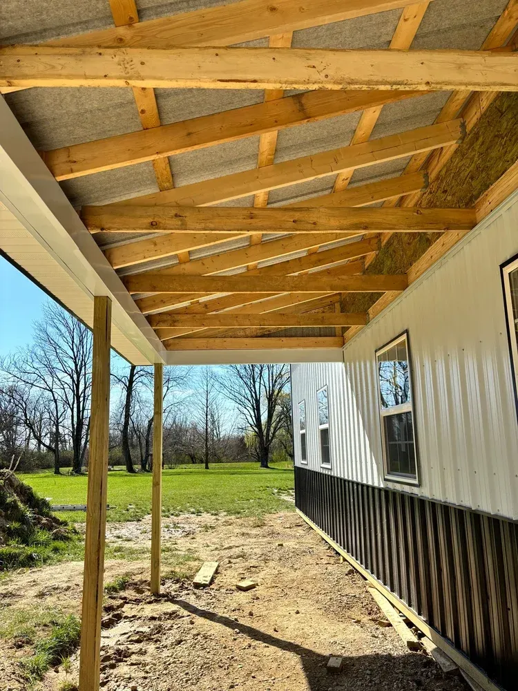 Construction of a white and dark metal building with a wooden porch roof.