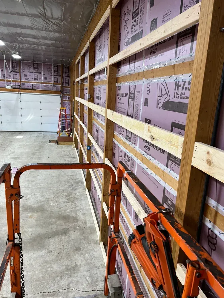 Construction of a garage interior with pink insulation, wooden beams, and an orange lift.
