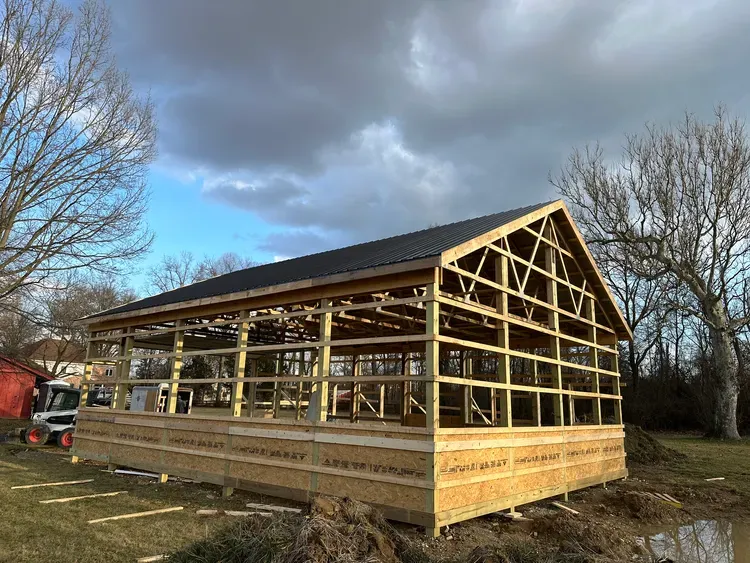 Wooden structure of a building under construction; brown frame, dark roof, outdoors, cloudy sky.