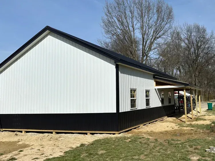 White and black metal building with a porch, under a blue sky.