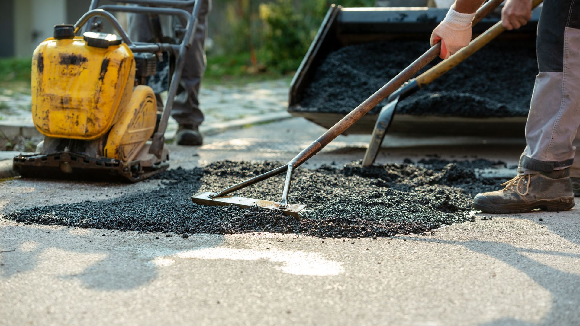 Construction workers in orange uniforms spread hot asphalt on a road with rakes.