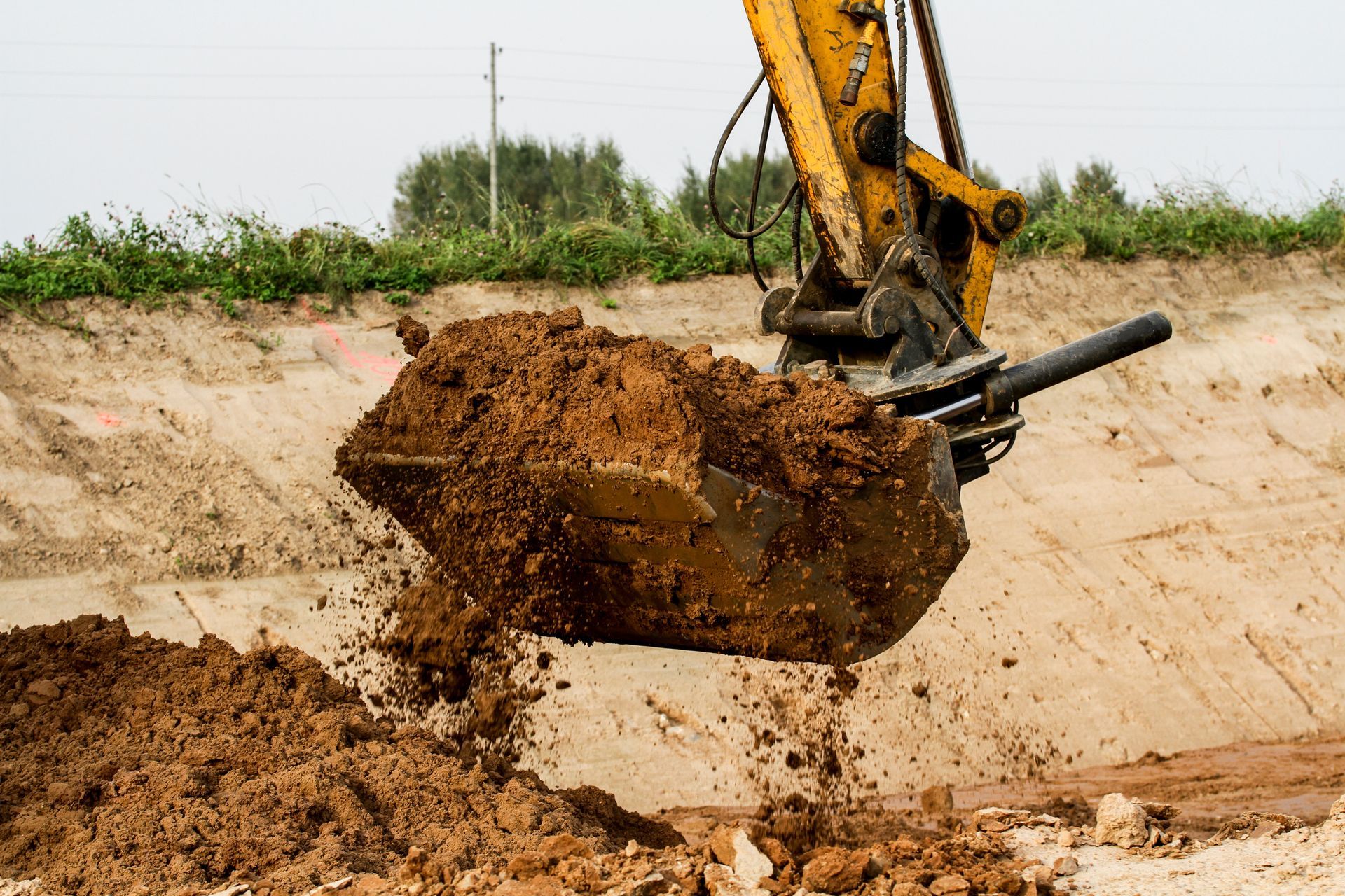 A yellow excavator bucket dumps a load of brown soil at a construction site.
