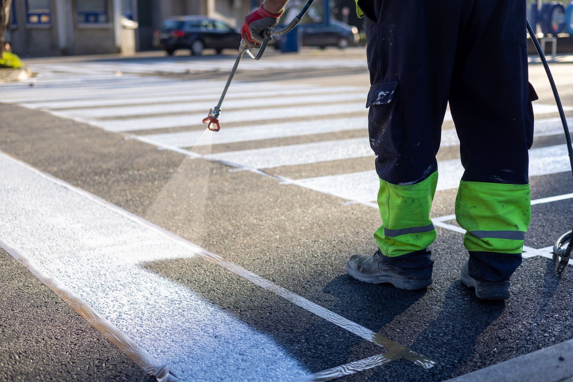 A worker sprays white paint onto a road to mark a pedestrian crosswalk.