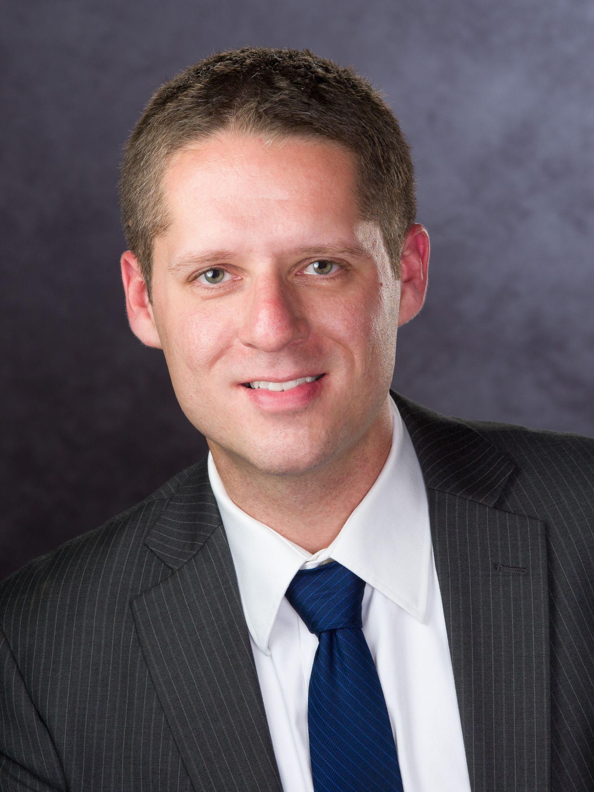 Bald man in a suit smiles at the camera, against a grey backdrop.