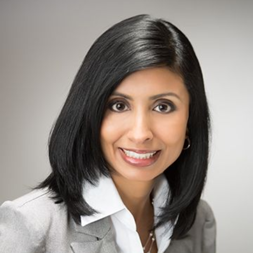 Bald man in a suit smiles at the camera, against a grey backdrop.