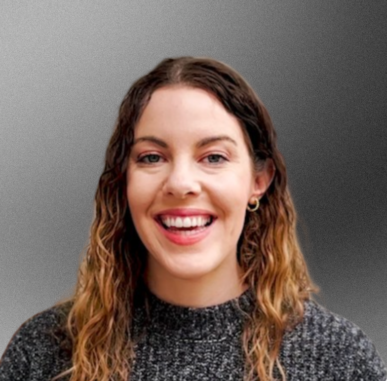 Woman with curly brown hair smiling widely, wearing a gray sweater.