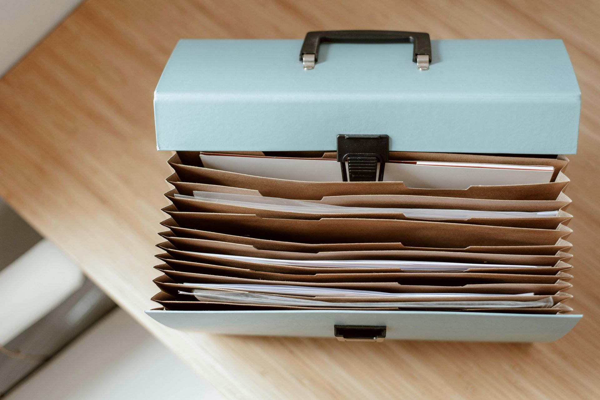 Blue accordion file folder on a wooden surface, filled with papers.